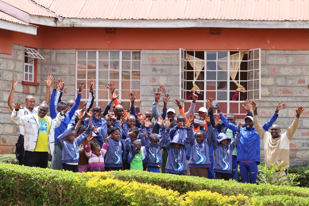 Academy players and staff in blue academy jackets raising their hands together outside a school