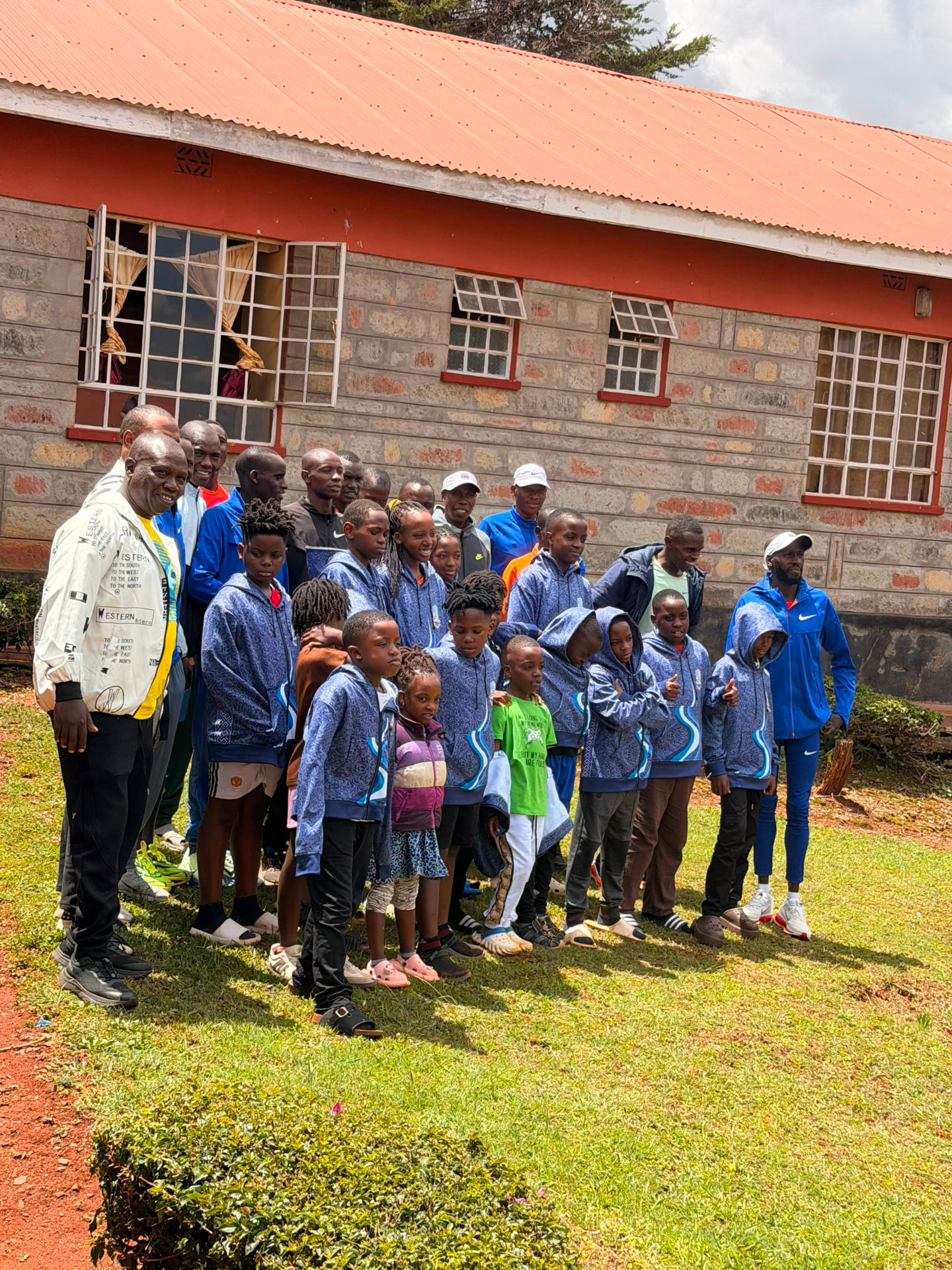 Large group of academy players and staff posing on the grass outside a school building